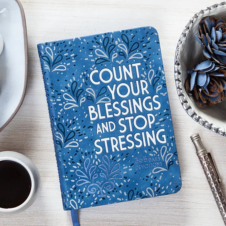 Blue notebook with 'Count your blessings and stop stressing' text on a desk with a cup of coffee and pen.