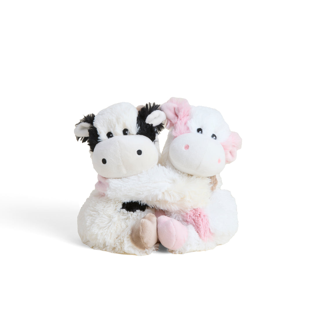 Two plush cow toys, one black and white and one pink, on a white background