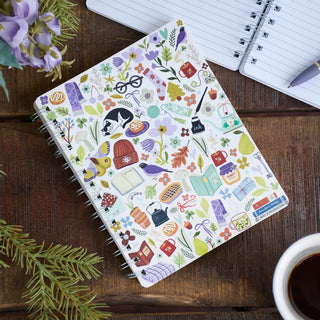 Notebook with colorful illustrations on a wooden surface with a cup of coffee and flowers.