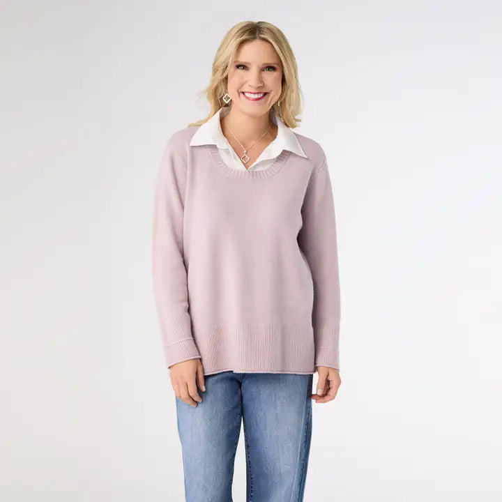 Woman wearing a light pink sweater with a white collar and blue jeans on a plain background