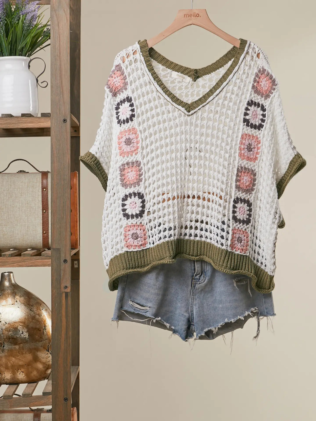 Crocheted top with floral patterns on a hanger against a neutral background