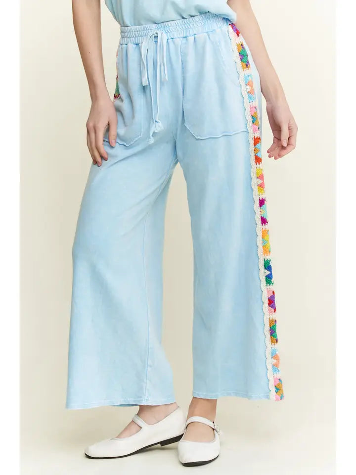 Light blue pants with colorful side stripe worn by a person on a white background