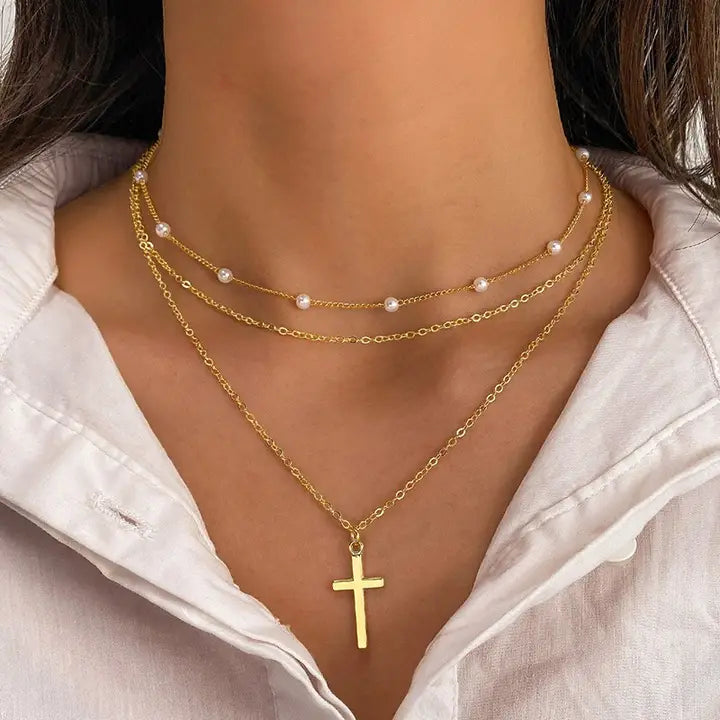 Gold necklaces with a cross pendant on a person wearing a white shirt.