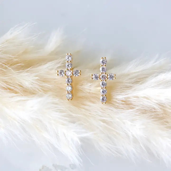 Gold cross earrings with clear stones on a fluffy white surface