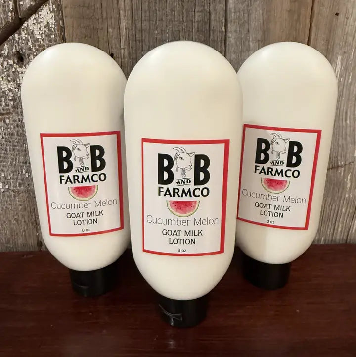 Three bottles of B&amp;B Farmco cucumber melon goat milk lotion on a wooden surface with a rustic background.