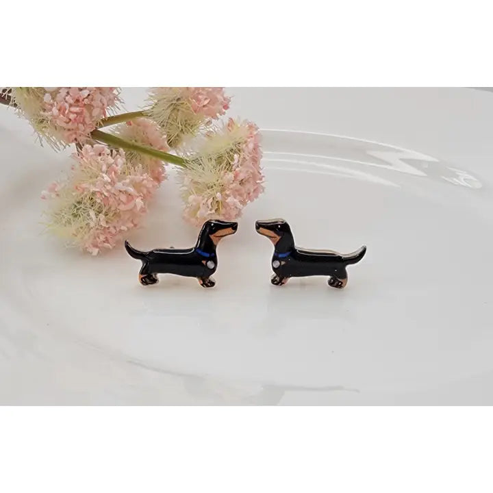 Black dachshund-shaped earrings on a white surface with pink flowers in the background