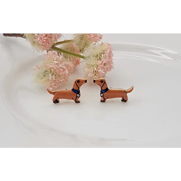 Pair of dachshund-shaped earrings on a white plate with pink flowers in the background