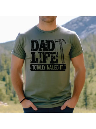 Person wearing a green t-shirt with 'Dad Life Totally Nailed It' text in a mountainous landscape.