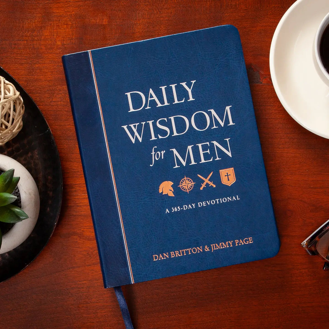 Blue book titled 'Daily Wisdom for Men' on a wooden table with a cup and decorative items.