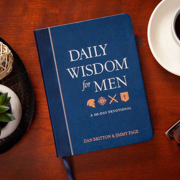 Blue book titled 'Daily Wisdom for Men' on a wooden table with a cup and decorative items.