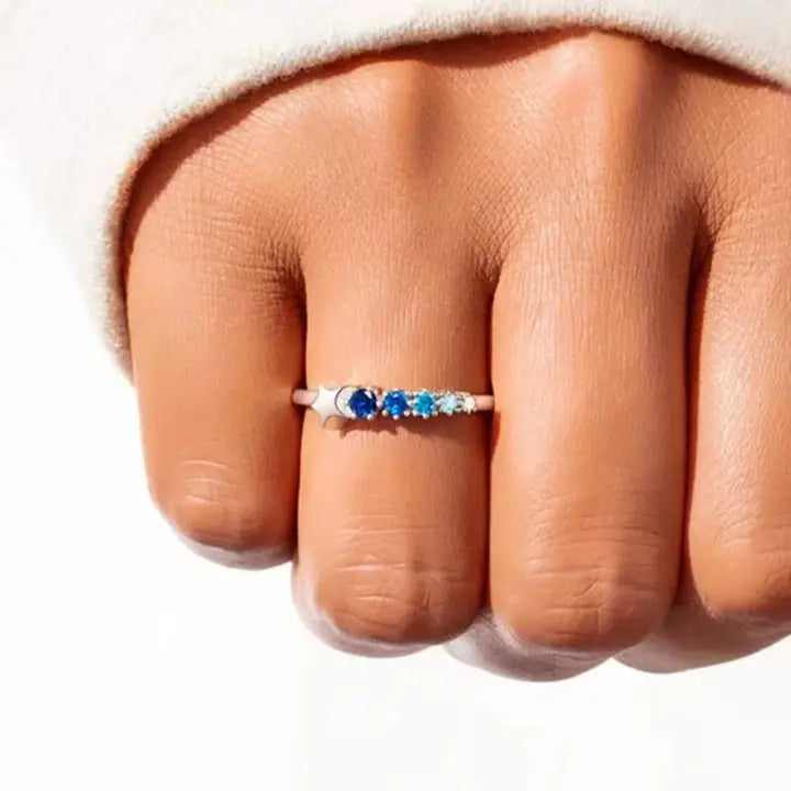 Close-up of a hand wearing a ring with blue and green gemstones on a white background