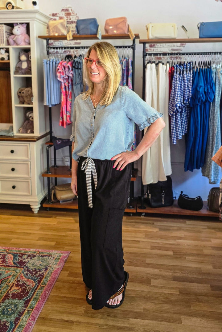 Woman standing in a clothing store with racks of clothes and shelves in the background.