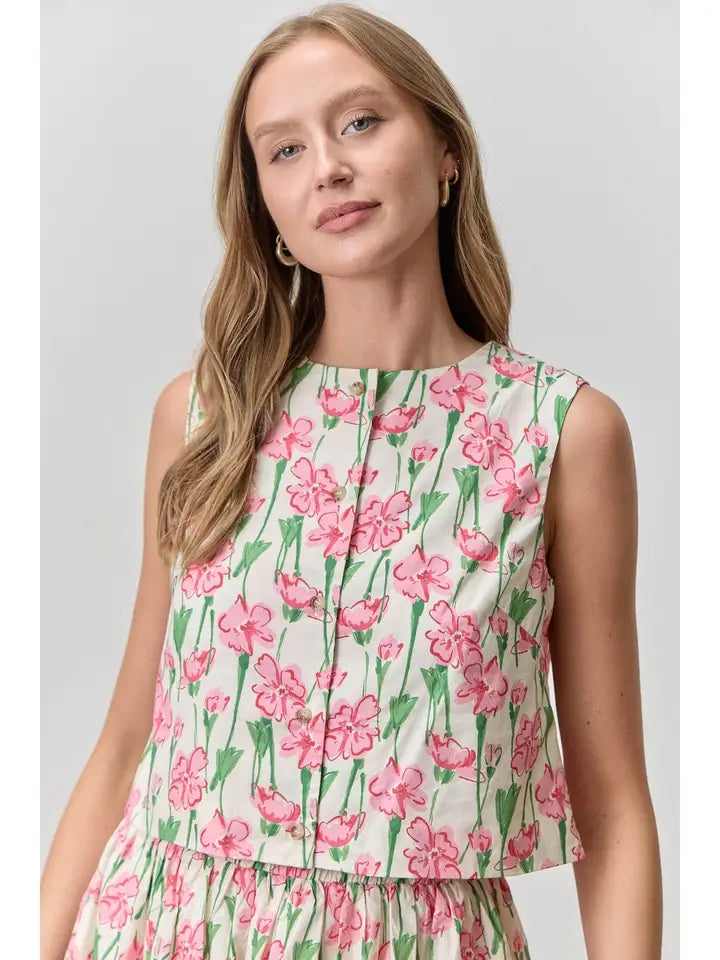 Woman wearing a sleeveless floral dress with pink flowers on a plain background