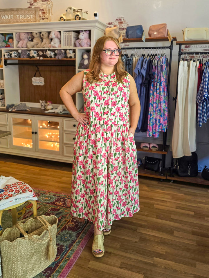 Woman in a floral dress standing in a store with clothing racks and displays.
