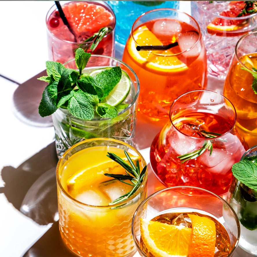Assorted colorful cocktails with garnishes on a white surface
