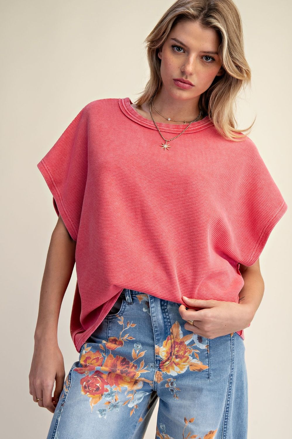 Woman wearing a pink poncho and floral jeans on a plain background