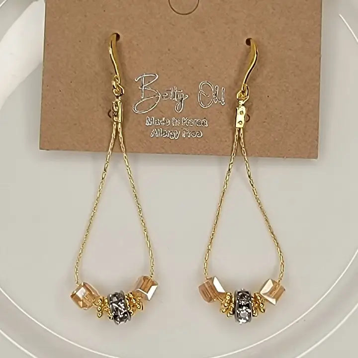 Gold earrings with beads on a white plate with a branded card in the background.