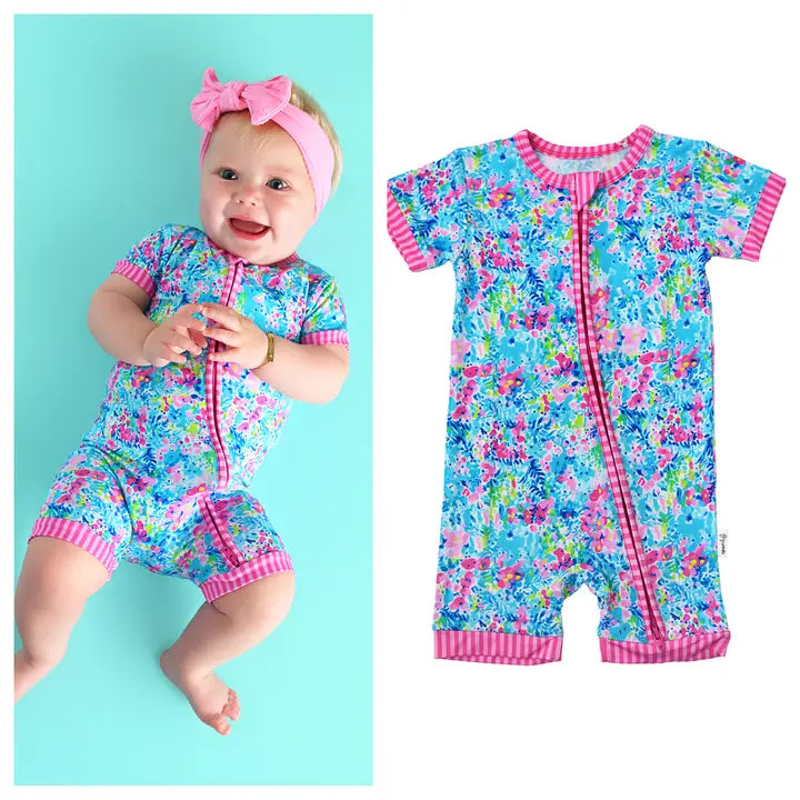 Baby wearing a colorful floral swimsuit with pink trim on a turquoise background