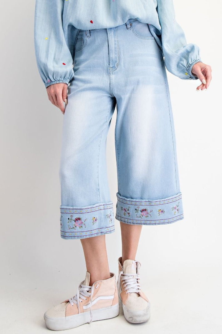 Person wearing light blue jeans with floral embroidery and a matching top on a plain background