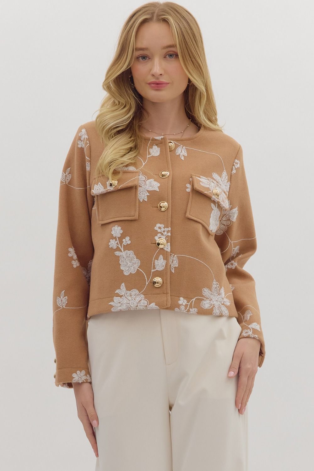 Woman wearing a brown floral embroidered jacket on a white background