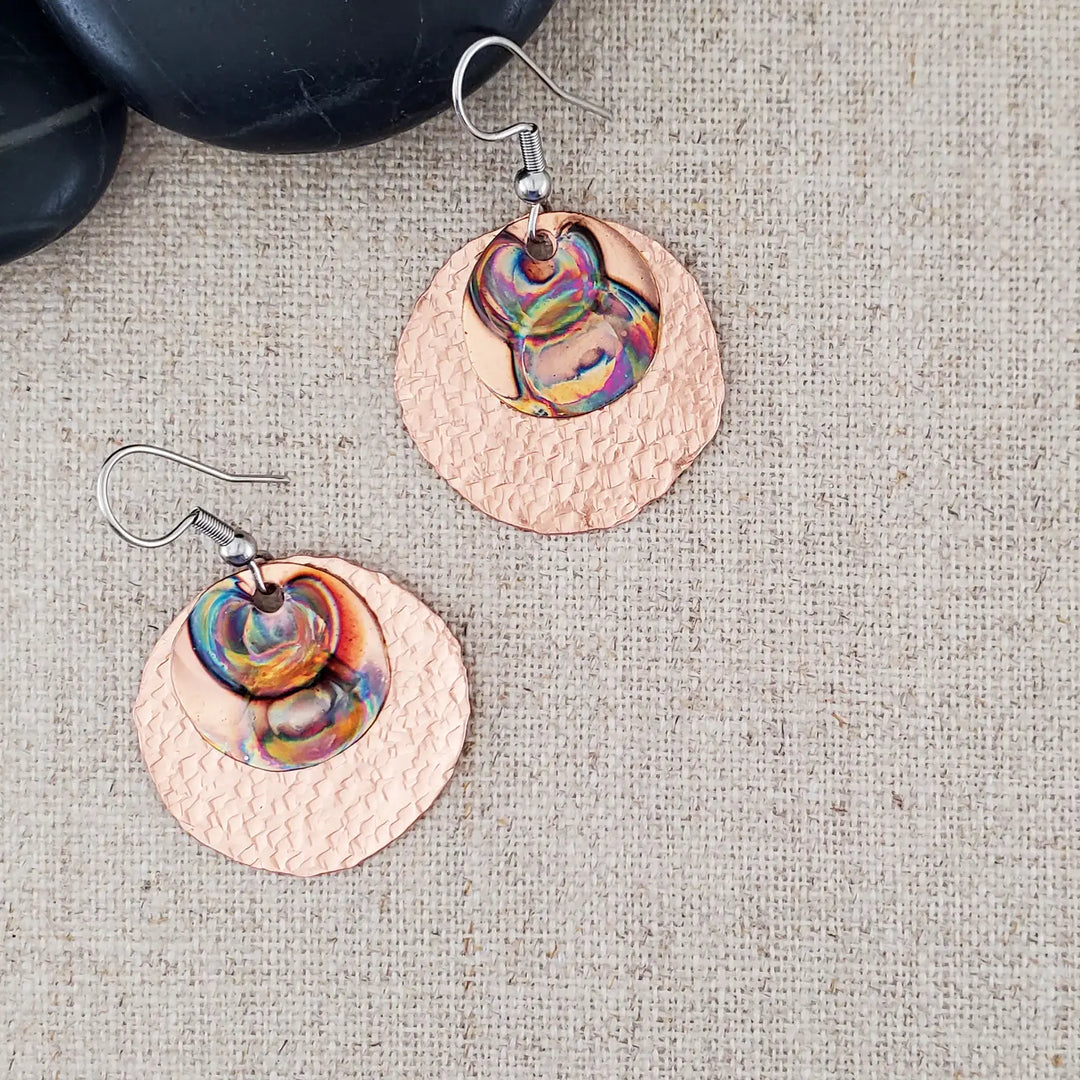Copper earrings with colorful interior on a textured fabric background