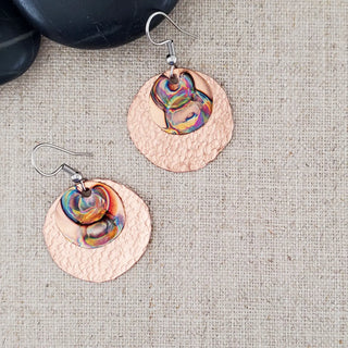 Copper earrings with colorful interior on a textured fabric background