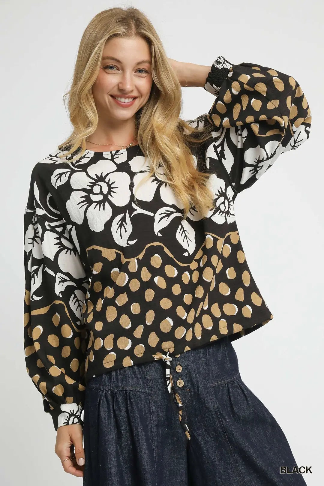 Woman wearing a black floral and polka dot top with a white background