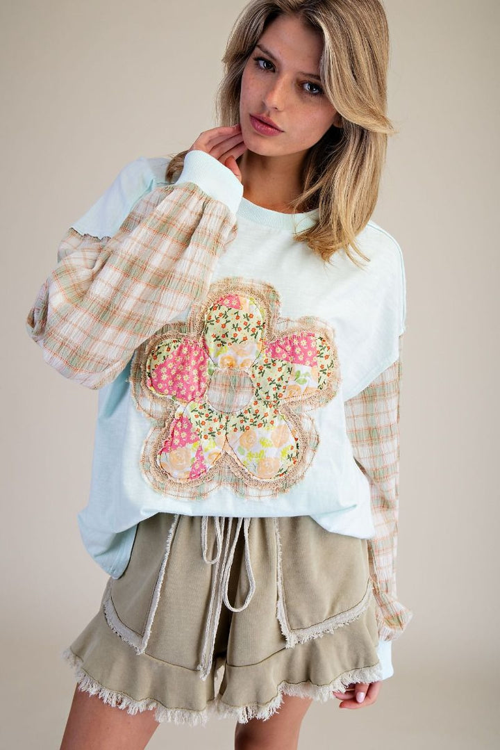 Woman wearing a white sweatshirt with a floral patch and beige shorts on a plain background