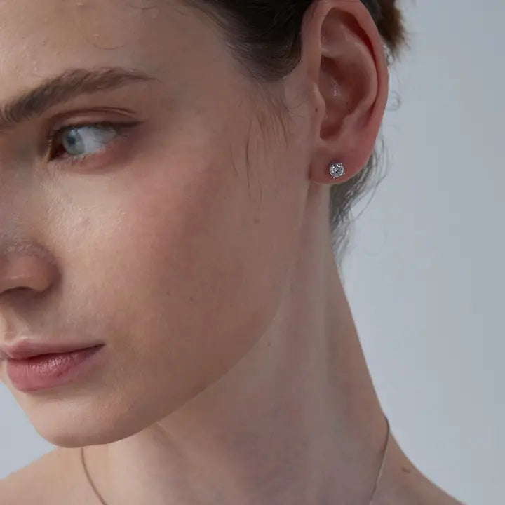 Close-up of a woman's face wearing a diamond earring against a neutral background