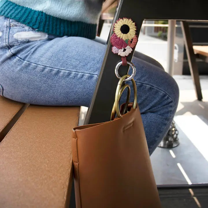 Brown leather handbag with floral keychain and keys, person sitting on a bench.