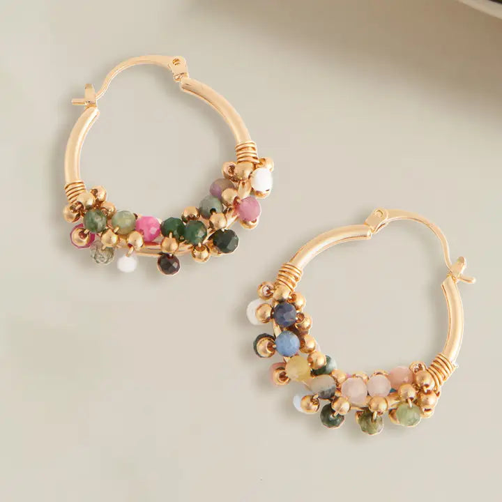 Gold hoop earrings with multicolored gemstones on a light background