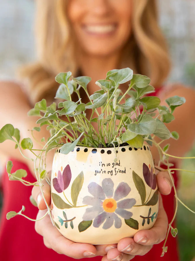Person holding a decorative plant pot with floral design and text.