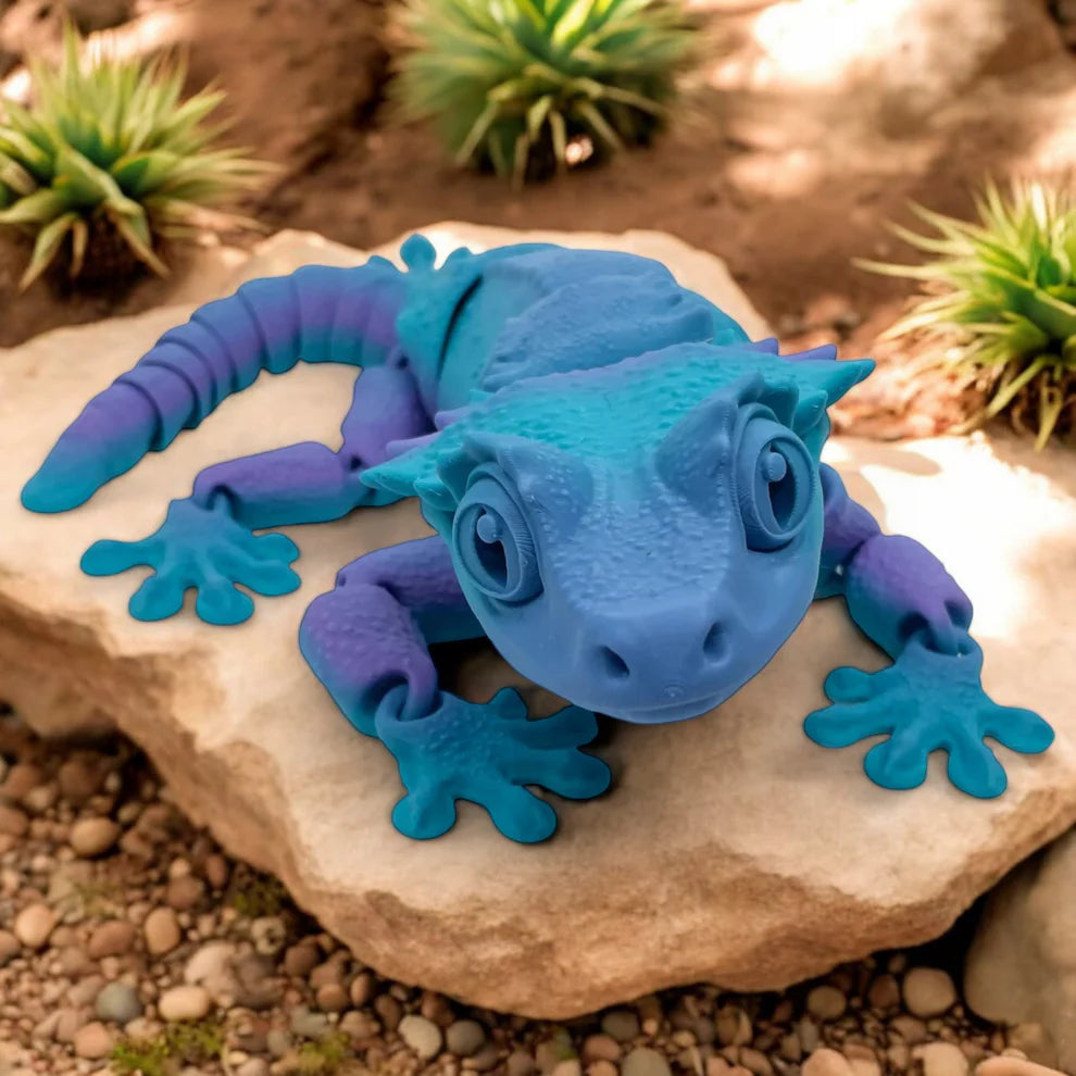 Blue and purple toy lizard on a rock with plants in the background