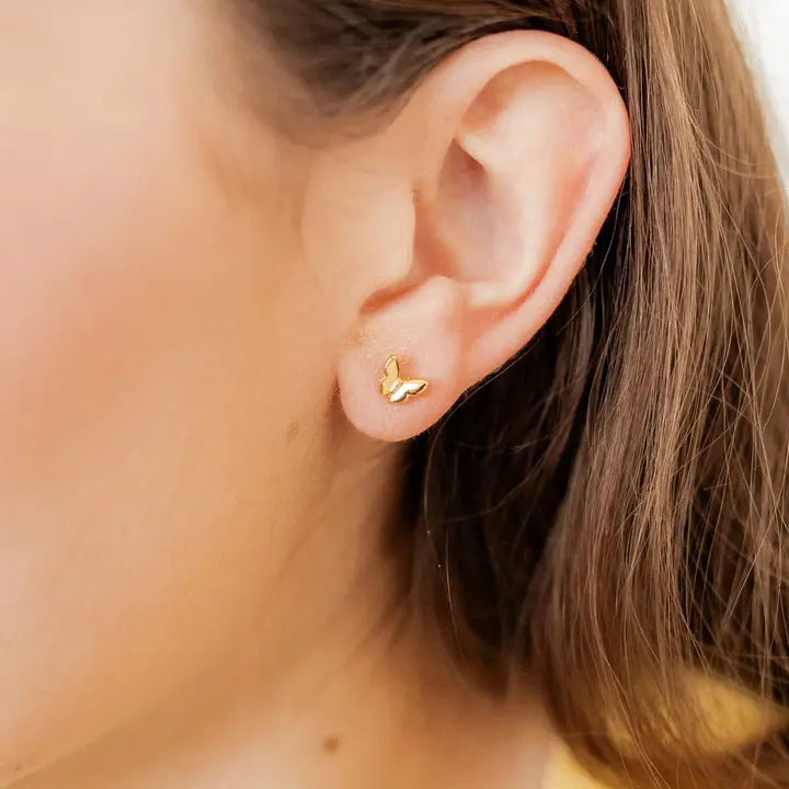 Gold butterfly earring worn by a person with blurred background