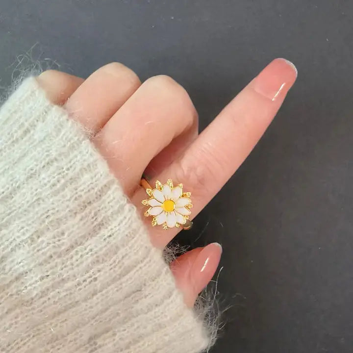 Hand wearing a daisy-shaped ring on a dark background
