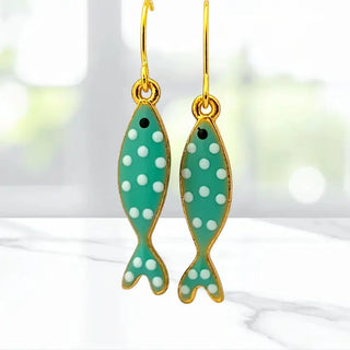 Green fish-shaped earrings with white polka dots on a blurred background