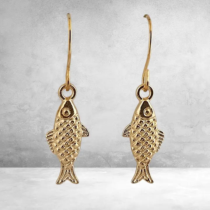 Gold fish-shaped earrings on a gray background