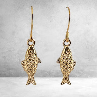 Gold fish-shaped earrings on a gray background