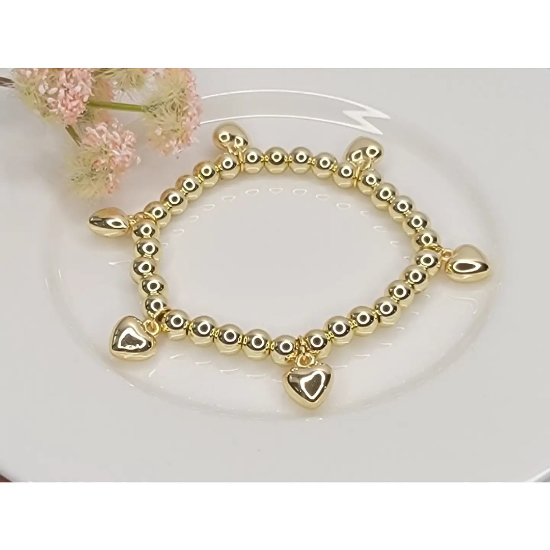 Gold beaded bracelet with heart charms on a white plate