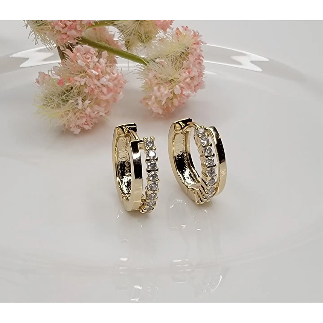 Gold hoop earrings with embedded stones on a white surface with pink flowers in the background