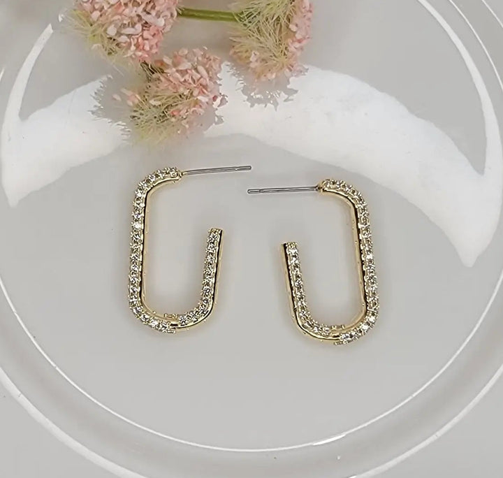 Gold hoop earrings on a clear glass surface with pink flowers in the background