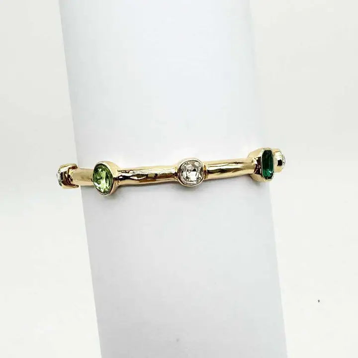 Gold bracelet with green and clear gemstones on a white background