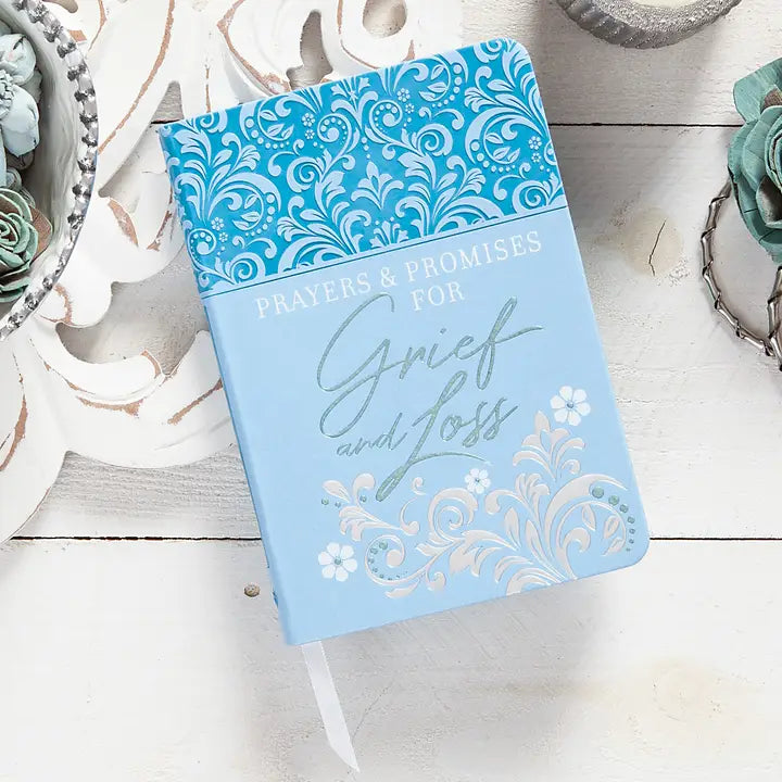 Blue journal titled 'Prayers & Promises for Grief and Loss' on a white surface with decorative elements.