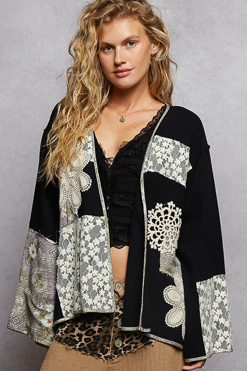 Woman wearing a black and white floral patterned jacket over a black top with a leopard print bottom on a gray background