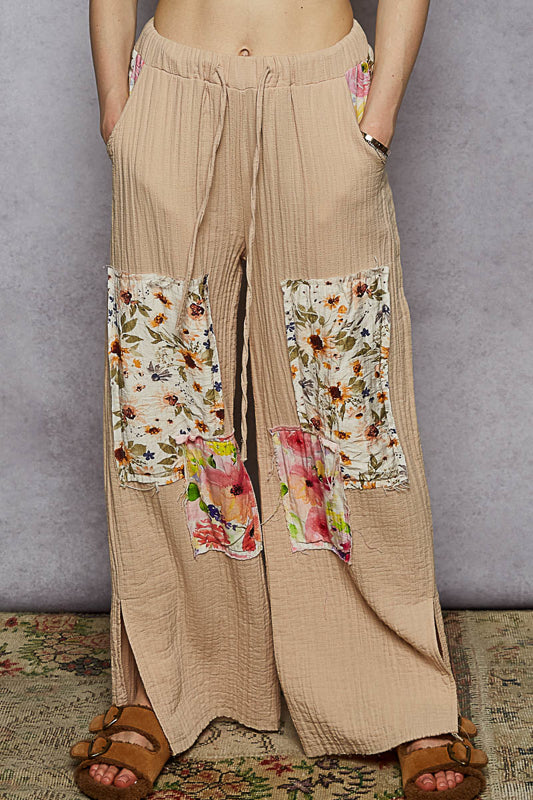 Beige wide-leg pants with floral patchwork on a gray background