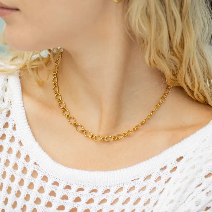 Gold chain necklace worn by a person with a white lace top