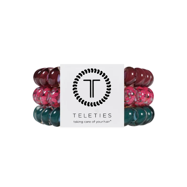 Three Teleties hair elastic bands in burgundy, pink, and teal-green translucent patterns, wrapped around a white paper band with the Teleties logo.