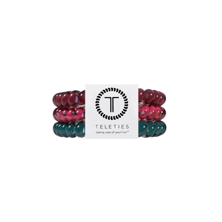 Three beaded stretch bracelets by Teleties, stacked vertically with a white paper band in the center. The top bracelet is dark burgundy, the middle is pink and red marbled, and the bottom is dark teal green marbled.