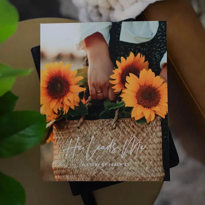 Book or notebook with sunflower design and 'He Leads Me' text on a blurred background