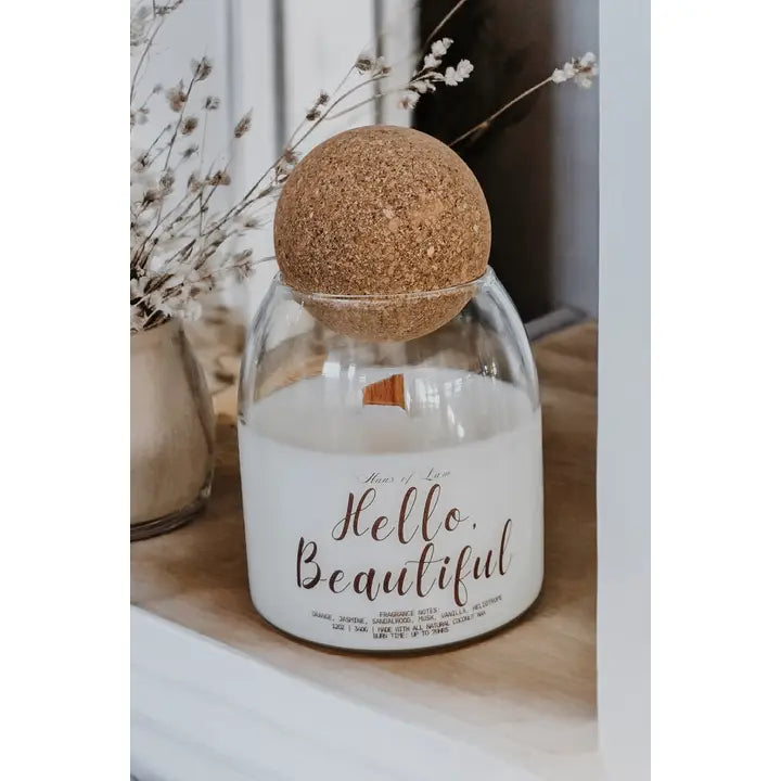 Candle in a glass jar with a cork lid on a wooden surface, surrounded by dried flowers.